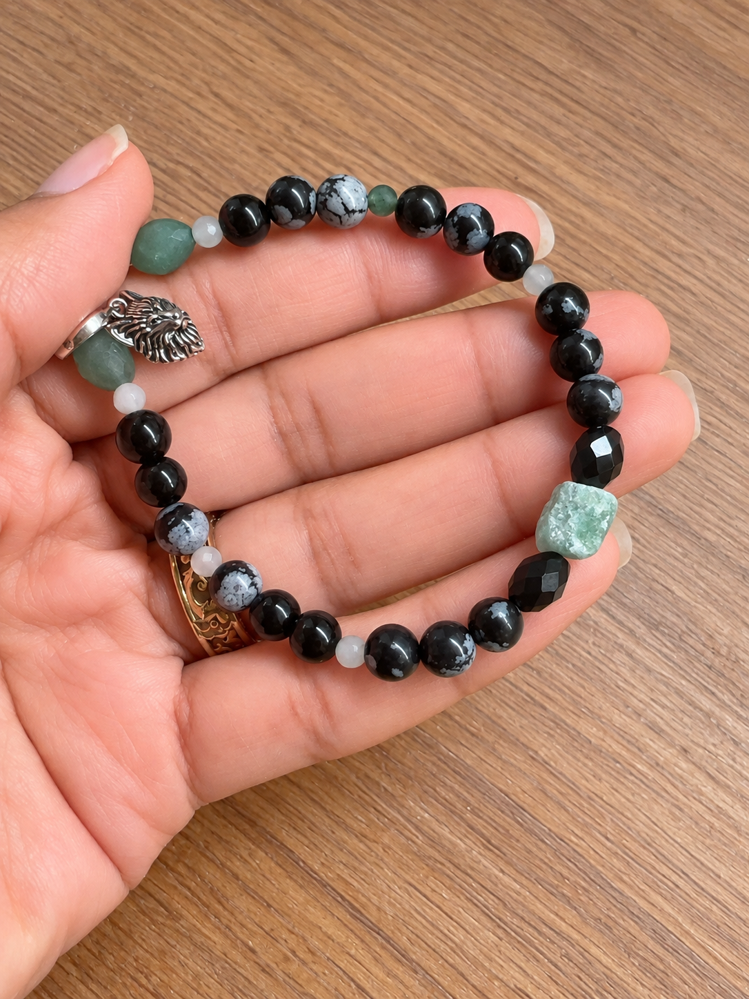 Le Gardien du Territoire, bracelet en aventurine verte et obsidiennes avec breloque loup, présenté dans la main